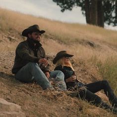 a man and woman sitting on the side of a hill