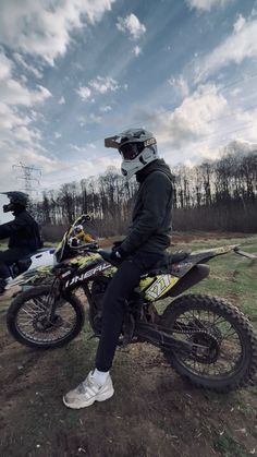 a man sitting on top of a dirt bike next to another person wearing a helmet