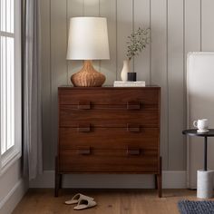 a lamp on top of a dresser next to a window with a pair of slippers