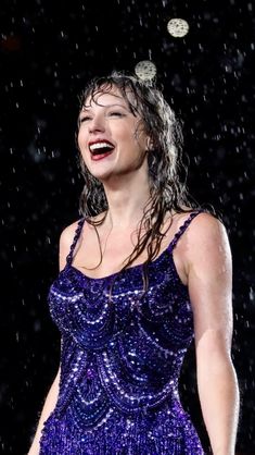 a woman in a blue dress singing on stage with rain falling over her head and hands behind her back