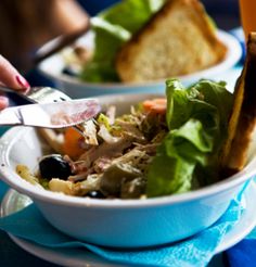 there is a salad in the bowl and bread on the plate next to it with a glass of orange juice