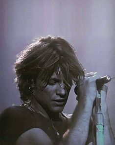 a man with long hair and no shirt on holding a microphone in his right hand