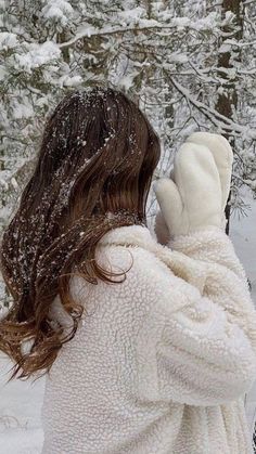 a woman standing in the snow with her back to the camera, wearing a white coat and mittens