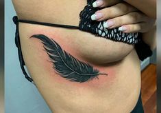 a woman's stomach with a black feather tattoo on her belly and the side