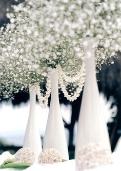 three white vases with baby's breath flowers in them sitting on a table