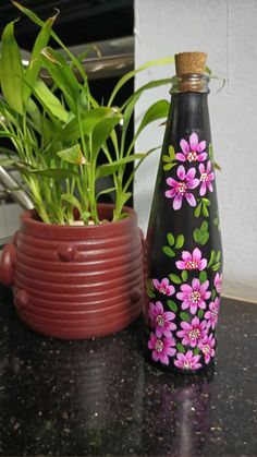 a black bottle with pink flowers painted on it sitting next to a red planter