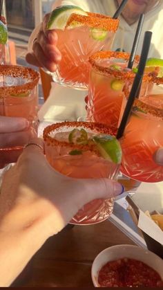 people holding up glasses filled with drinks and garnished with limes on the rim