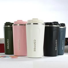 four different colored coffee cups lined up on a white table with their lids down and one has a straw in it