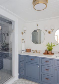 a bathroom with blue cabinets and gold fixtures on the countertop, along with a round mirror