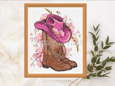 a cross stitch picture of a cowboy boot and pink hat with flowers in the background