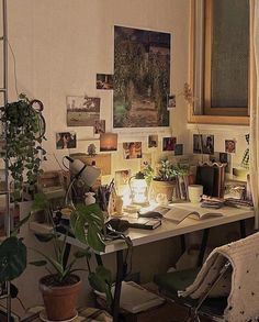 a desk with plants and pictures on the wall next to a chair in front of a window