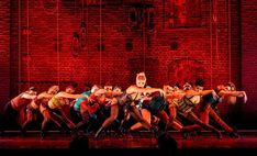 a group of dancers on stage in front of a brick wall with red light behind them