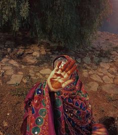 a woman with her hands in the air while sitting on some rocks and dirt near a tree