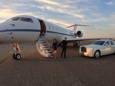 two people standing in front of a private jet on the tarmac next to a limousine