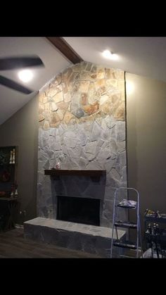 a living room with a stone fireplace in the center and a ceiling fan above it