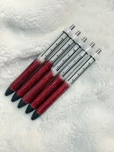 six red and black stilettos are lined up on a white blanket with silver tips