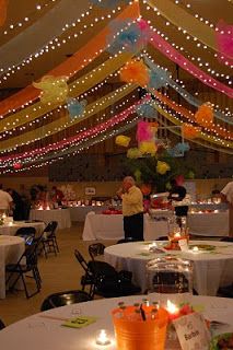 an indoor event with many tables and chairs covered in balloons, streamers and lights