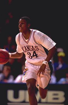 a young man dribbling a basketball during a game in front of an audience