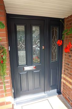 a black front door with two glass panels and red flowers on the side walk next to it