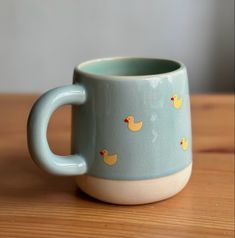 a blue mug with yellow ducks on it sitting on top of a wooden table next to a wall