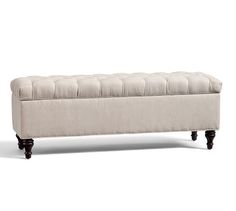 an upholstered bench with wooden legs and tufted cushion on the top, in front of a white background