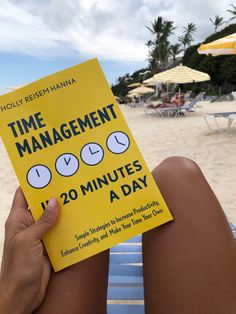 a person sitting on a beach holding up a book with the title time management 120 minutes a day