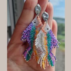 a pair of colorful fish shaped beaded earrings in the palm of someone's hand