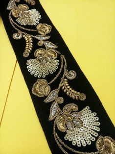 a black tie with gold embroidered flowers and leaves on it's side, sitting on a yellow surface