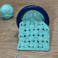 a close up of a knitted object on a wooden surface with yarn in the background