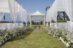 an outdoor wedding setup with white flowers and draping on the grass, surrounded by greenery