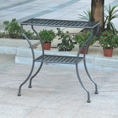 a small metal table sitting on top of a sidewalk next to potted planters