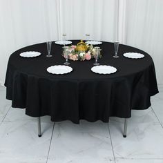 a black table topped with white plates and wine glasses next to a vase filled with flowers