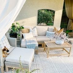 an outdoor living area with couches, chairs and tables on the patio covered in white curtains