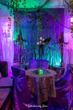 a table with purple cloths on it in front of a decorated wall and couches