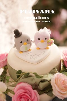 two small birds sitting on top of a wedding cake with pink roses around it and the words fujiiyama creations above them