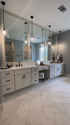 a large bathroom with two sinks and three mirrors on the wall, along with several lights hanging from the ceiling