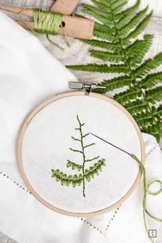 a cross stitch pattern with a fern leaf on it and some green thread next to it