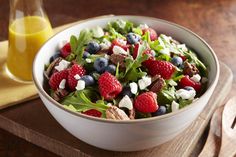 a white bowl filled with salad and berries on top of a wooden cutting board next to a glass of orange juice