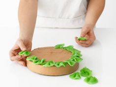 a person is decorating a cake with icing and green leaves on the top