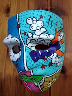 a blue mask with cartoon characters on it sitting on top of a wooden floor next to a pair of scissors