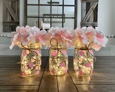 three mason jars filled with pink flowers on top of a wooden table