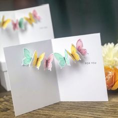 two greeting cards with butterflies on them sitting next to some yellow and pink flowers in front of a white card that says for you