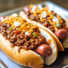 two chili dogs with cheese and onions on a silver platter, ready to be eaten