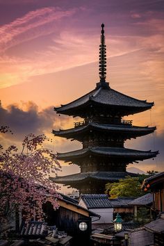 a tall pagoda with trees in the foreground and clouds in the sky above it