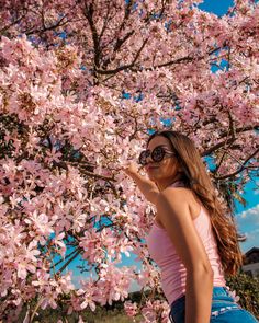 a woman standing under a tree with pink flowers