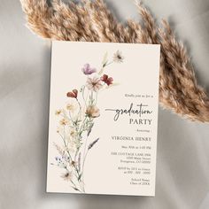 a wedding party card with wildflowers and grasses on the front, sitting next to some dried grass