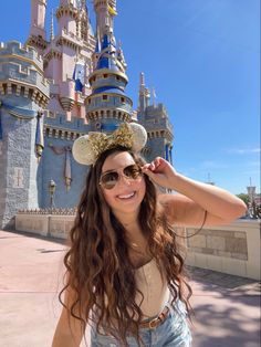 a woman wearing sunglasses and a mouse ears hat in front of a castle at disneyland