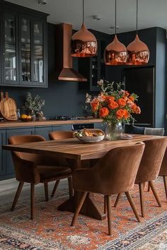 a dining room table surrounded by chairs and vases with orange flowers on it in front of blue cabinets