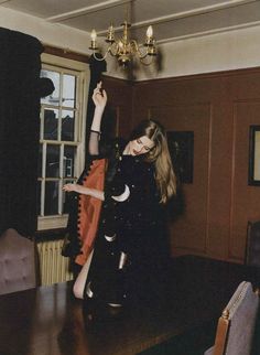 a woman standing on top of a wooden table in front of a chandelier