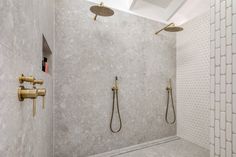 a bathroom with two shower heads and gold faucets on the wall, next to a walk in shower